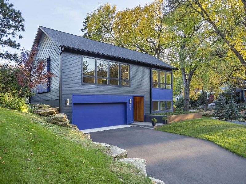 Front of modern single gable home painted black with vibrant blue details