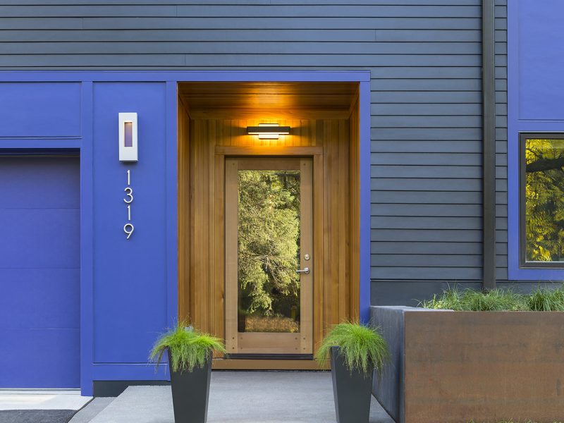 Front entrance to house showing warm wood paneled entry in contrast to cool blue and black painted exterior
